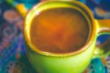 Close-up of a hand holding a vibrant, patterned ceramic cup filled with steaming coffee.