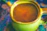 A close-up of a vibrant hand-thrown ceramic mug filled with steaming tea on a wooden table.