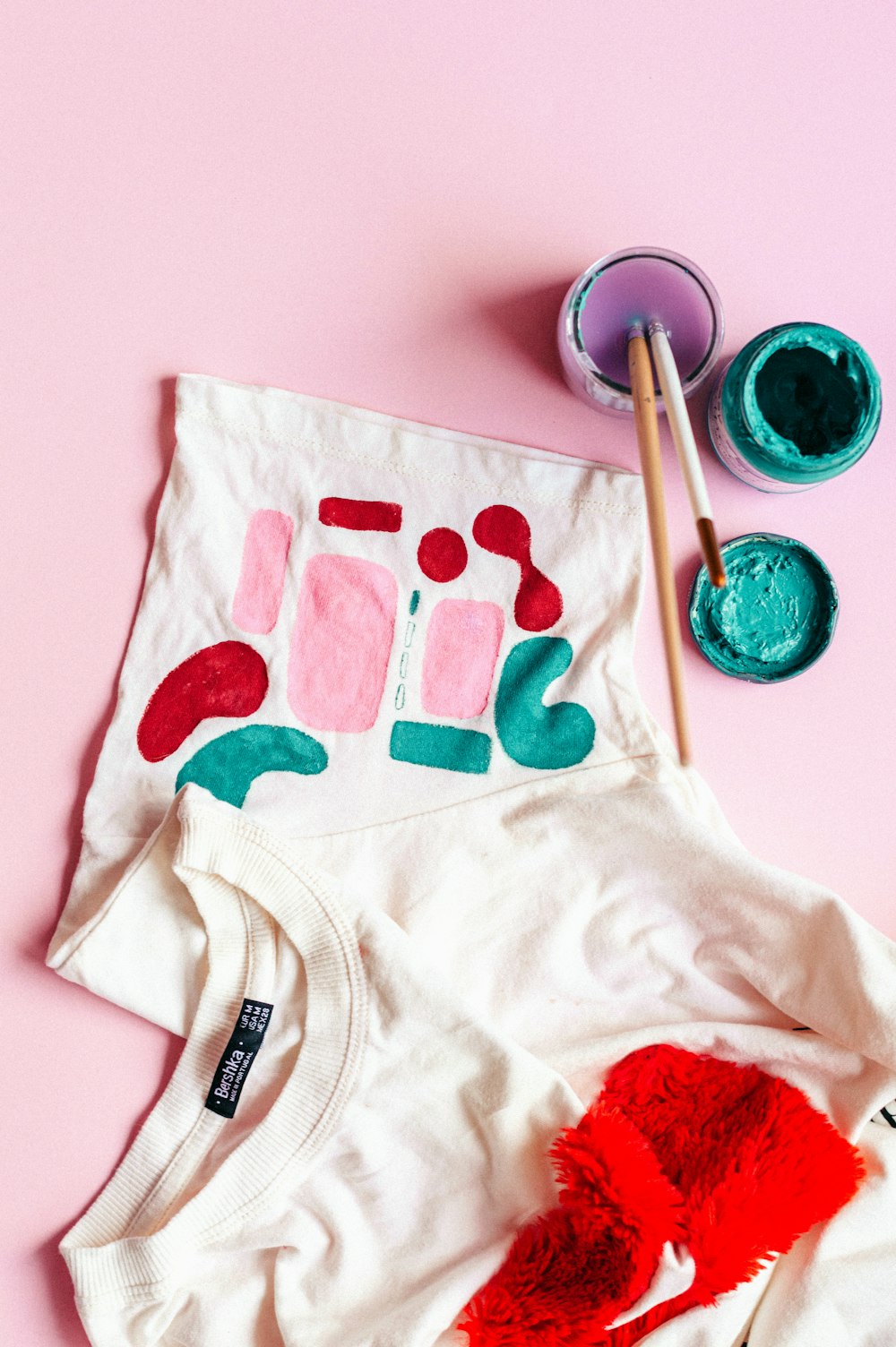 white and red crew-neck shirt beside paint with brushes