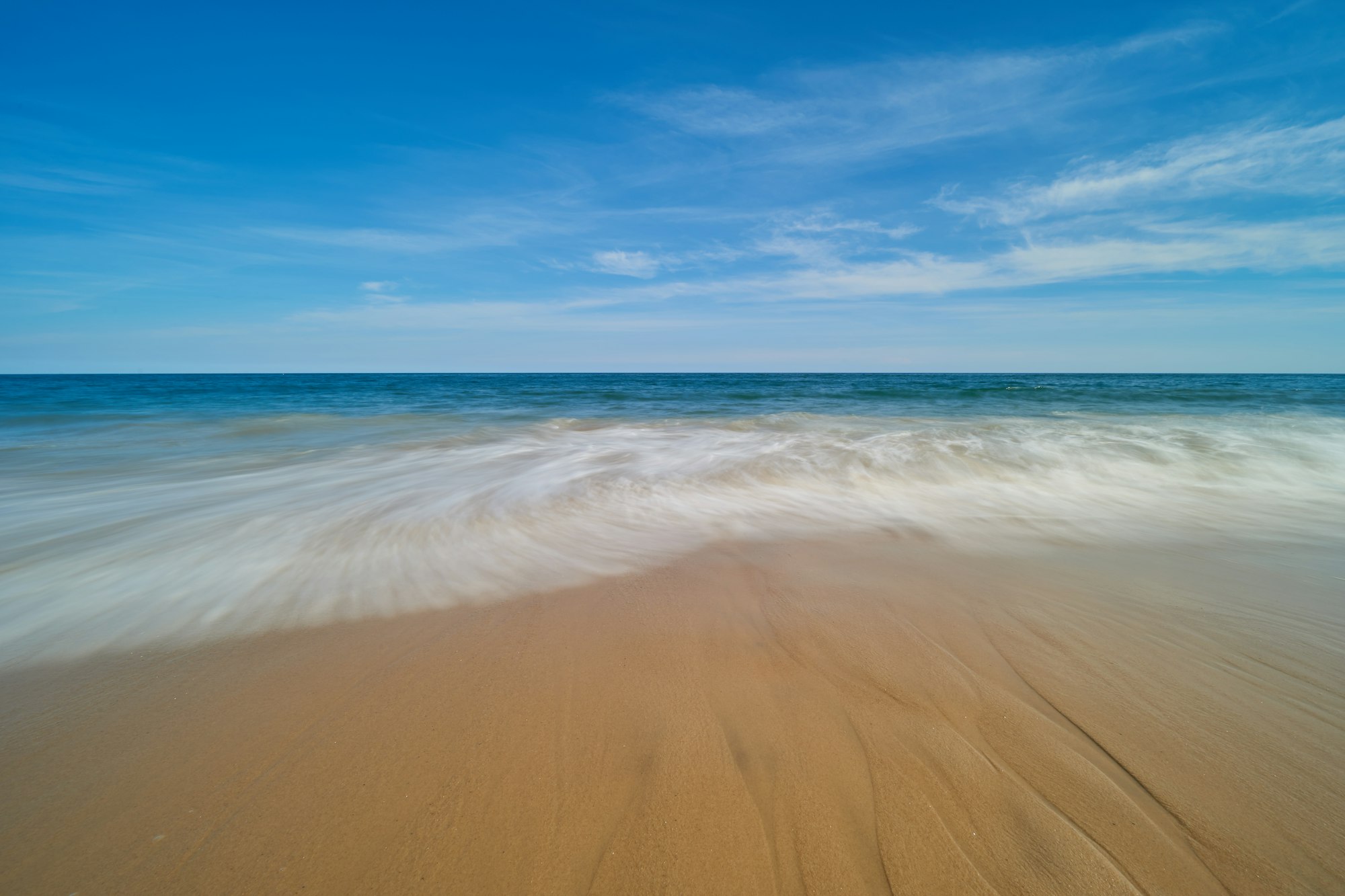 A sandy beach with waves and blue sky