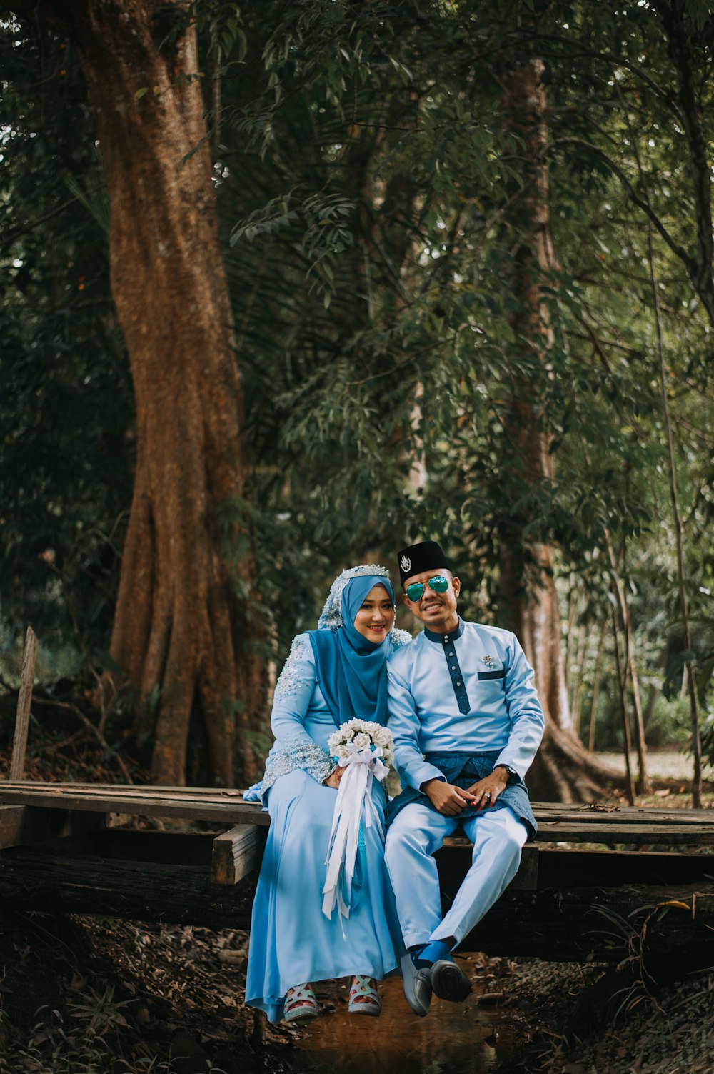 two wedding couple in blue outfit sitting on log