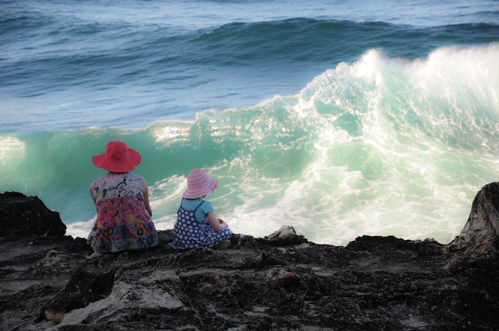 woman and girl sitting on cliff overlooking sea