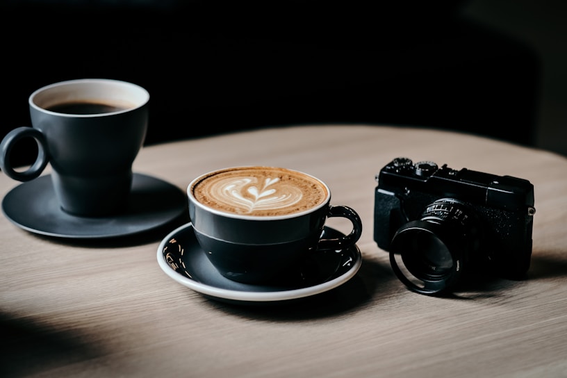 A cozy morning scene with a steaming cup of espresso beside a Sony A7 IV camera on a wooden table.