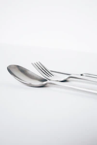 A close-up of a stylish spoon and fork set resting on a rustic wooden table with soft natural light.