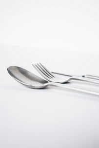 Close-up of polished silver spoons and forks resting on a textured wooden table with soft natural light
