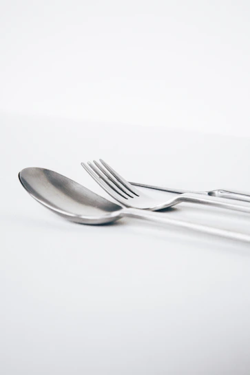A close-up of a stylish spoon and fork set resting on a rustic wooden table with soft natural light.