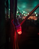 A close-up of a glowing red LED light attached to several cables, set against a dimly lit background with blurred vibrant green and blue lights in the distance.