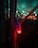 A close-up of a glowing red LED light attached to several cables, set against a dimly lit background with blurred vibrant green and blue lights in the distance.