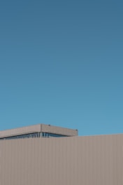 A minimalist architectural structure with linear patterns on its facade against a clear blue sky.