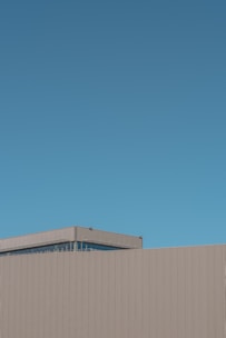 A minimalist architectural structure with linear patterns on its facade against a clear blue sky.