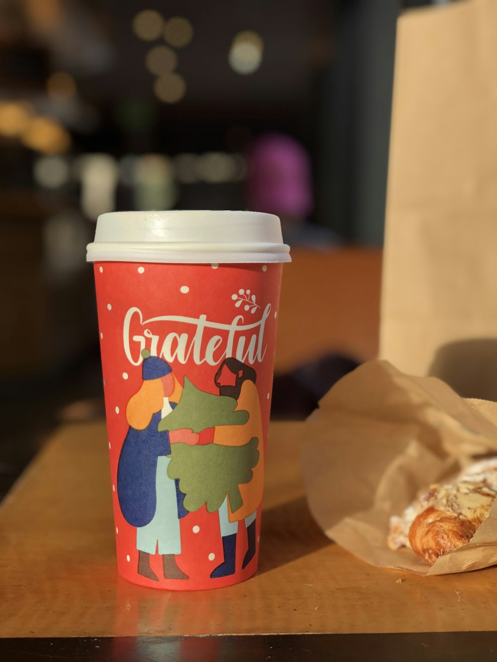 red and multicolored grateful disposable cup with lid near pastry on table