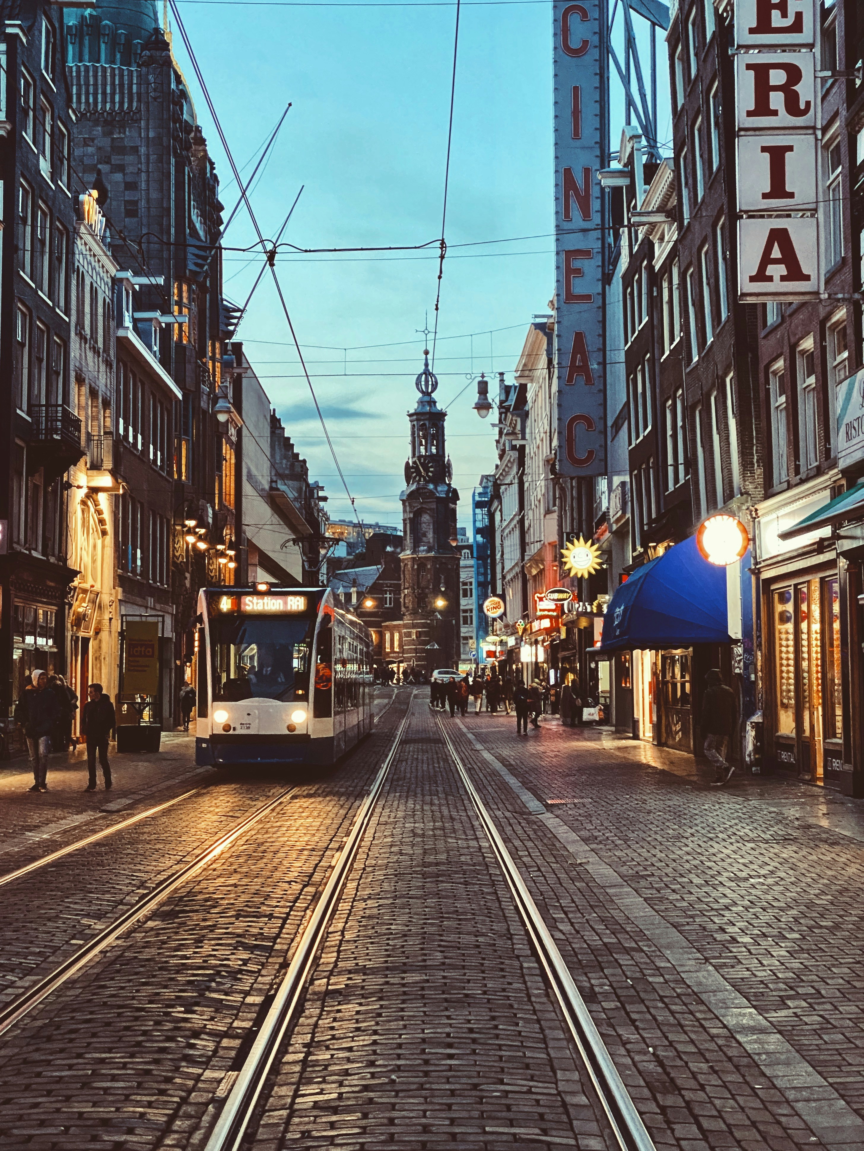 people walking on sidewalk with a tram passing by