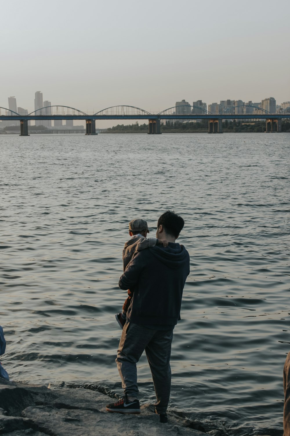 man carrying baby standing on boulder near body of water