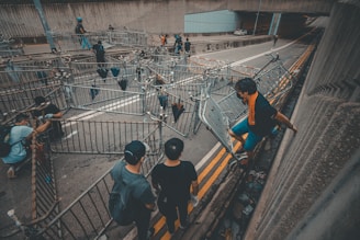 Several people are seen climbing and moving metal barricades on a road under a bridge or elevated structure. The scene appears organized but chaotic, with individuals systematically positioning the barriers. Most people are wearing dark clothing.