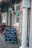 A building exterior with stone walls is adorned with colorful triangular banners. A blackboard sign outside advertises activities like pool and darts, as well as a courtyard garden with beer prices. Hanging flower baskets with vibrant blooms add to the festive atmosphere.