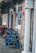 A building exterior with stone walls is adorned with colorful triangular banners. A blackboard sign outside advertises activities like pool and darts, as well as a courtyard garden with beer prices. Hanging flower baskets with vibrant blooms add to the festive atmosphere.