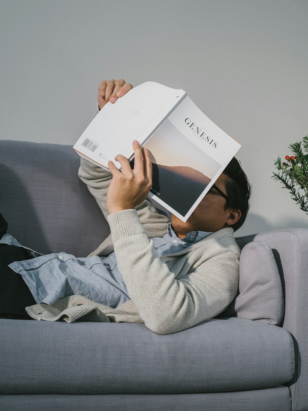 man reading book while lying on gray fabric sofa