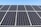 A field of solar panels is positioned under a clear blue sky. The panels are arranged in rows, capturing sunlight efficiently. The sleek, reflective surface of the panels gives a modern and clean look.