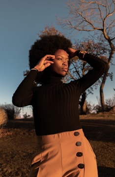 A stylish model posing outdoors with a cityscape background during golden hour.