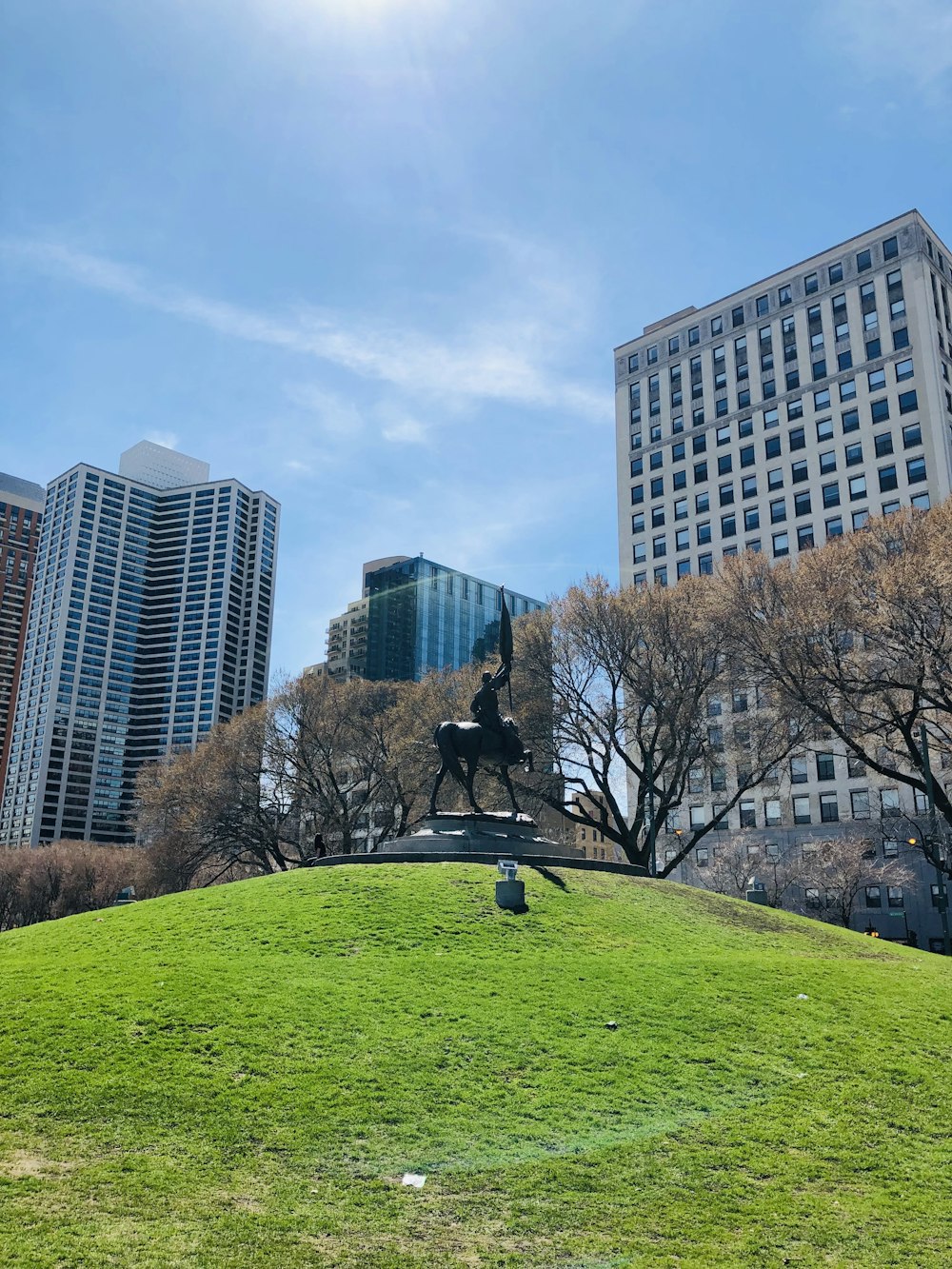 man riding horse statue beside trees and high-tise building