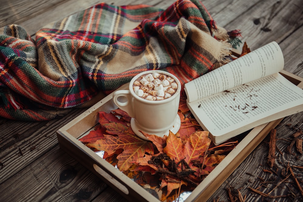 taza de café con malvavisco frente a un libro abierto en una bandeja