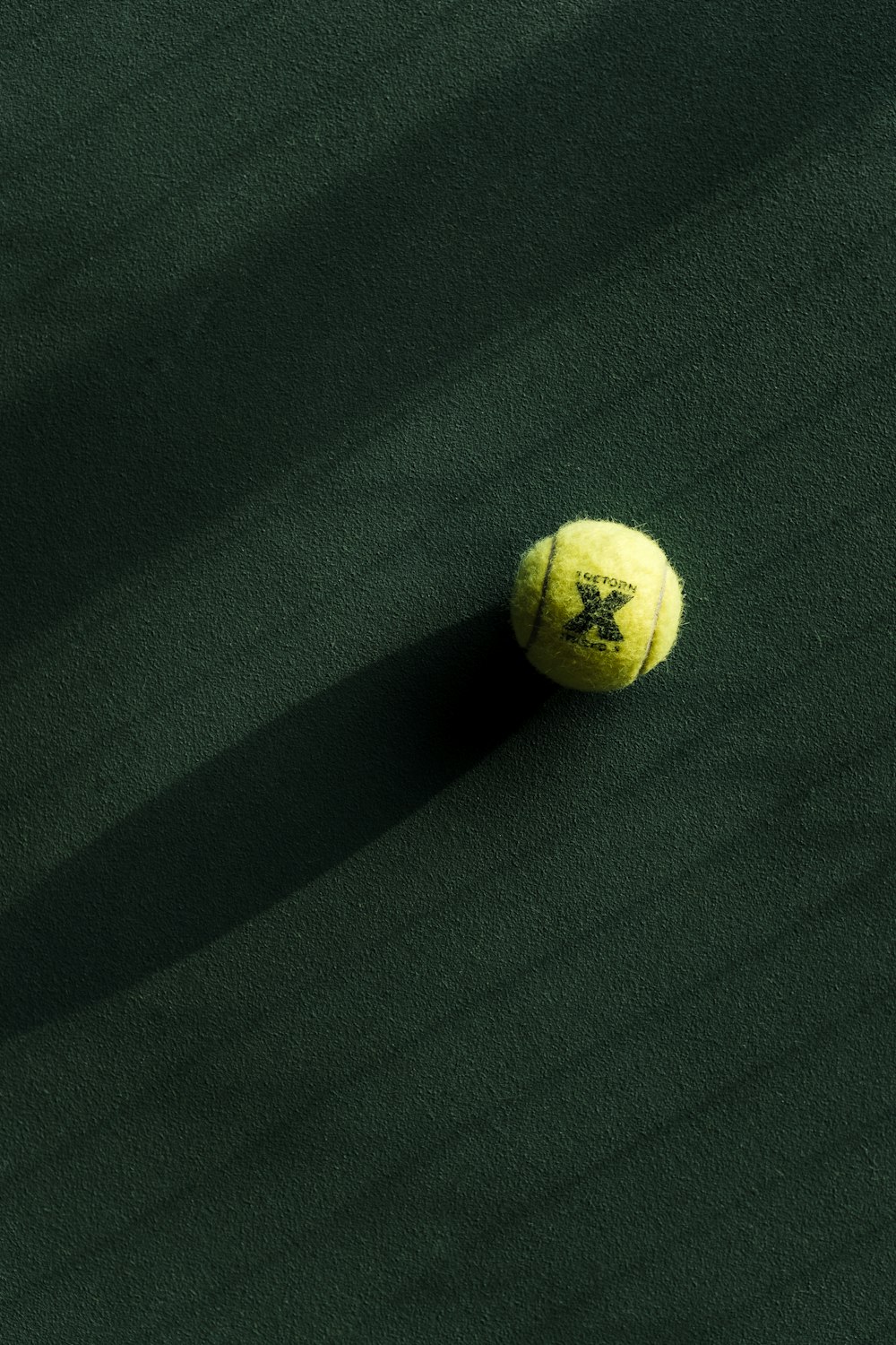 Una pelota de tenis en una cancha verde con una sombra