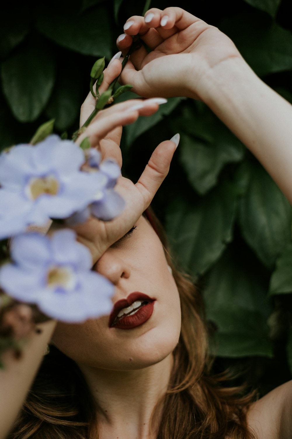 woman wearing red lipstick covered by blue petaled flower