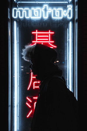 A lone figure silhouetted against a flickering neon sign, evoking isolation.