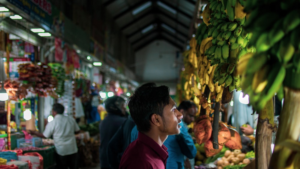 man in red shirt standing near green banana fruit during daytime