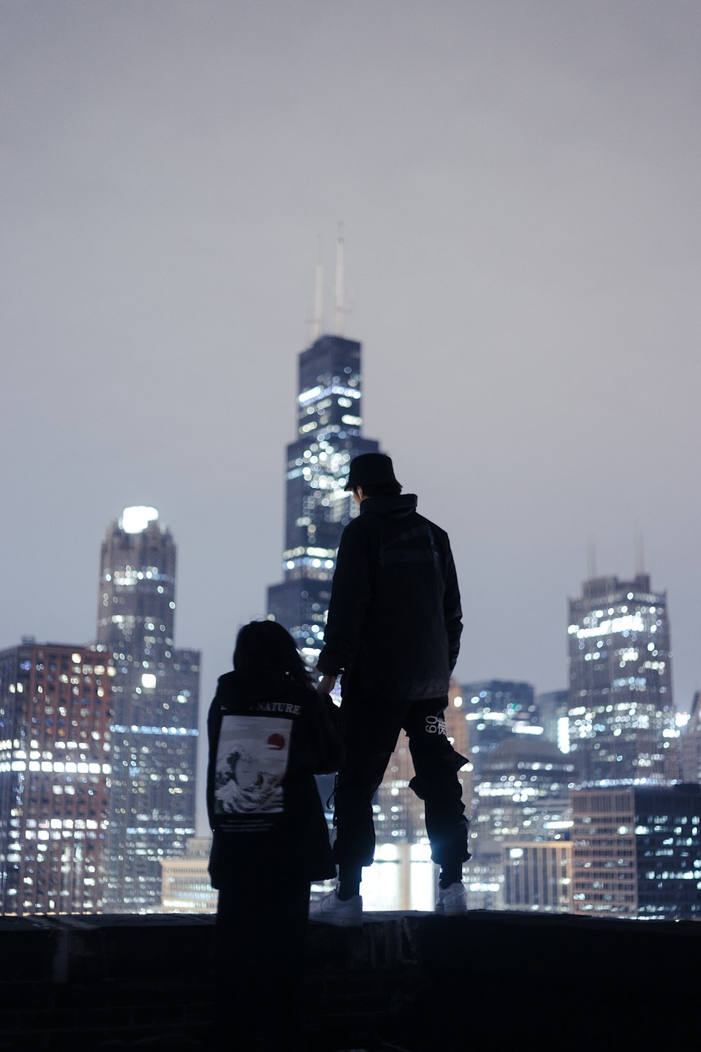 Silhouettenfotografie von zwei Personen, die in der Nähe der Kante mit Blick auf Hochhäuser stehen