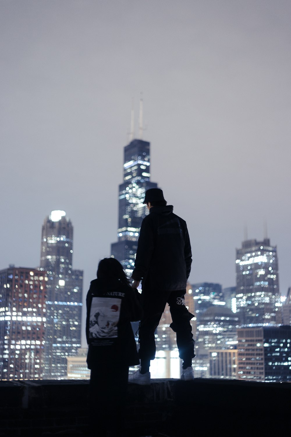 silhouette photography of two person standing near edge overlooking high-rise buildings