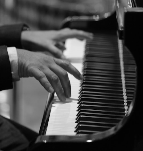 grayscale and selective focus photo of person playing piano