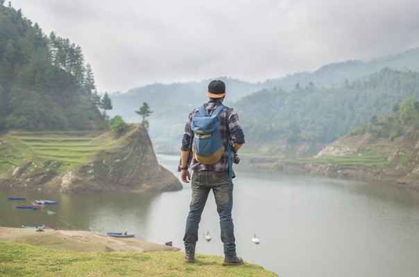 person in blue denim pants carrying blue backpack in front of body of water during daytime
