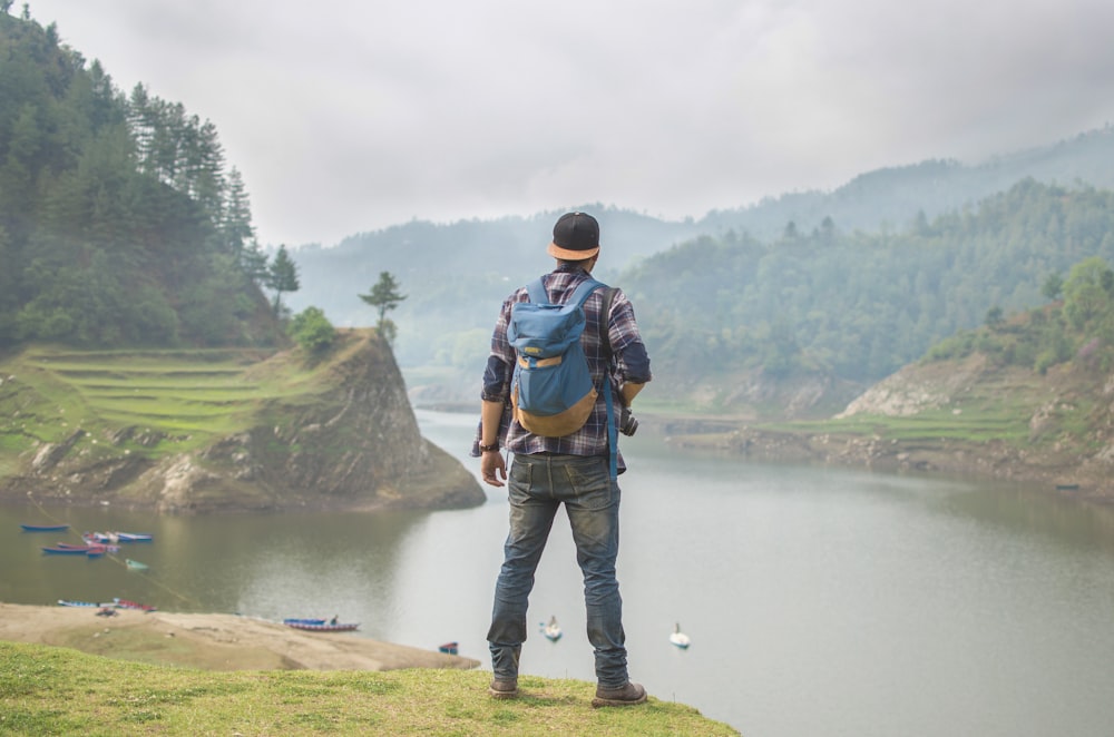 Personne en pantalon en jean bleu portant un sac à dos bleu devant un plan d’eau pendant la journée