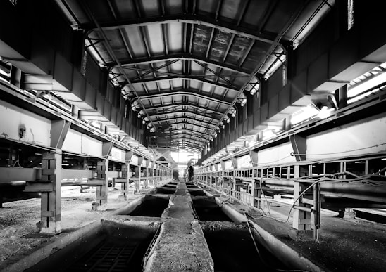 Black and white industrial photo showing steel beams stacked neatly in a warehouse.