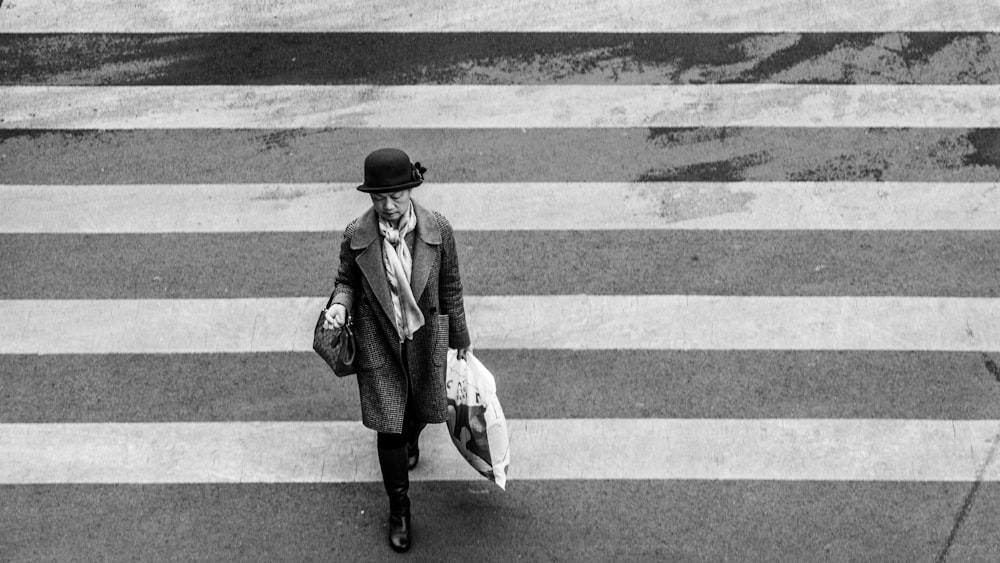 grayscale photo of person in trench coat crossing street