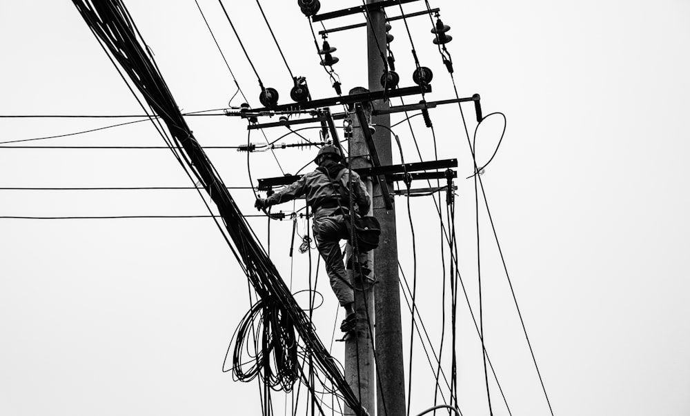 grayscale photo of person climbing electric post