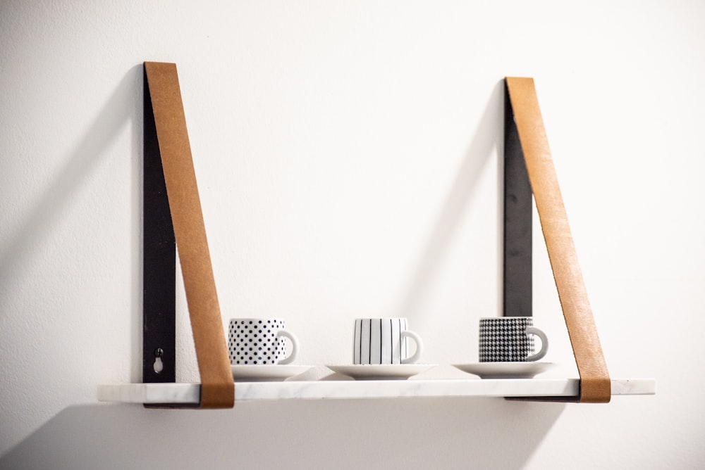 three white-and-black ceramic mugs with saucer on floating shelf