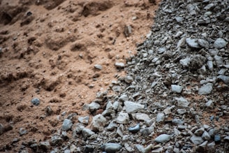 A close-up view of a mix of fine brown sand transitioning into a pile of gray rocks and pebbles, suggesting contrasting textures.