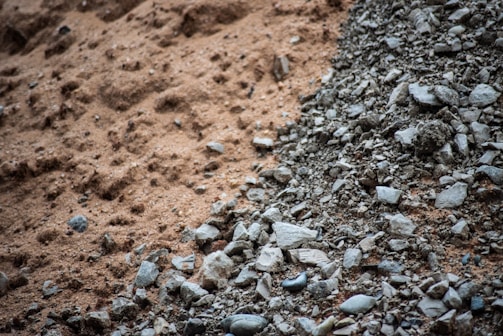 A close-up view of a mix of fine brown sand transitioning into a pile of gray rocks and pebbles, suggesting contrasting textures.