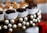 An arrangement of chocolate pieces wrapped in white paper cups is set on a decorative circular platter adorned with pearl-like beads. The chocolates are neatly aligned, and some are topped with nuts. The composition is elegant, with a focus on luxurious presentation.