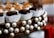 An arrangement of chocolate pieces wrapped in white paper cups is set on a decorative circular platter adorned with pearl-like beads. The chocolates are neatly aligned, and some are topped with nuts. The composition is elegant, with a focus on luxurious presentation.