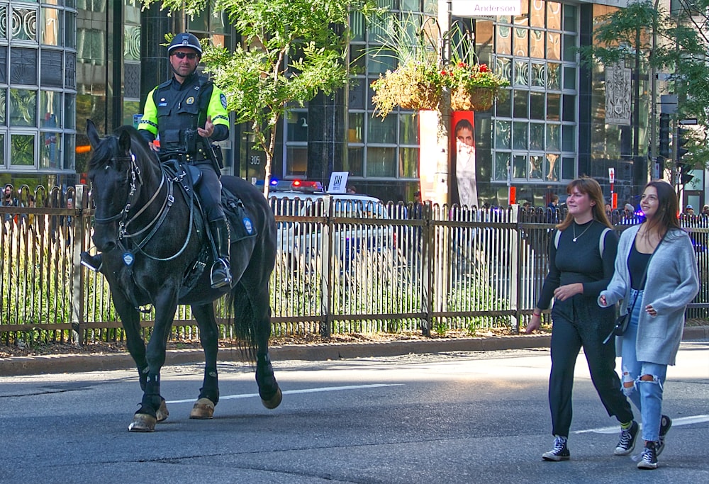 Polizist reitet auf Pferd neben zwei gehenden Frauen