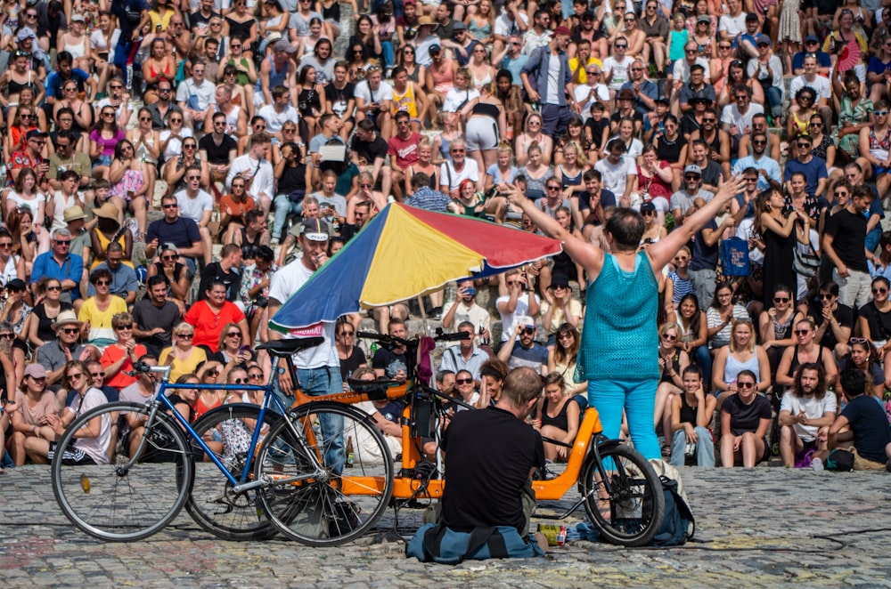 photography of two men standing beside bicycles in front of people during daytime