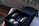 A neatly arranged set of black skincare bottles and jars inside an elegant black box. The box also contains rolled-up grey towels. The setting includes a wooden surface and a blurred background, creating a luxurious atmosphere.