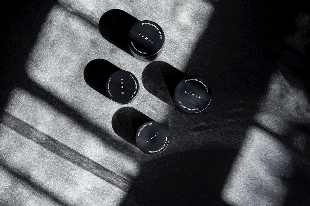 four black cream jars on gray surface