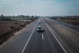 A highway stretching into the horizon with a fleet of trucks driving in formation.