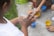 Children engaging in a creative activity outdoors, hands smudged with paint. Several containers with colorful paints are on the ground, and a child is seen mixing paint on their hands, focusing intently on the activity.