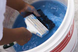 A craftsman’s hand stirring a bucket of thick white paint, ready for application.