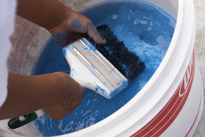 A craftsman’s hand stirring a bucket of thick white paint, ready for application.